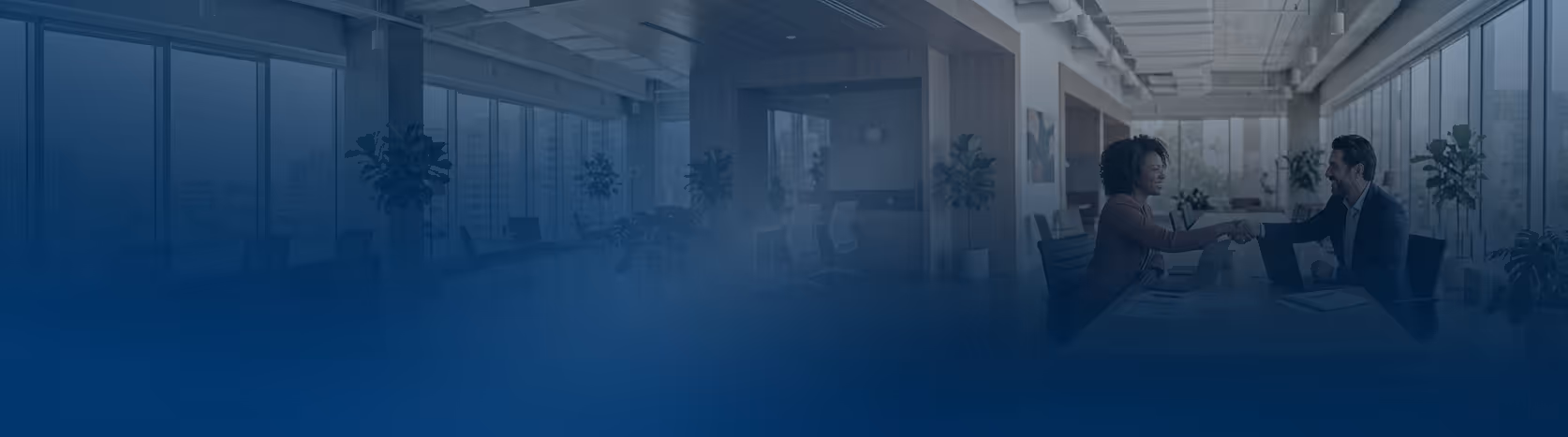 Dwóch ludzi uściski dłoni w biurze podczas spotkania przy stole z laptopami.