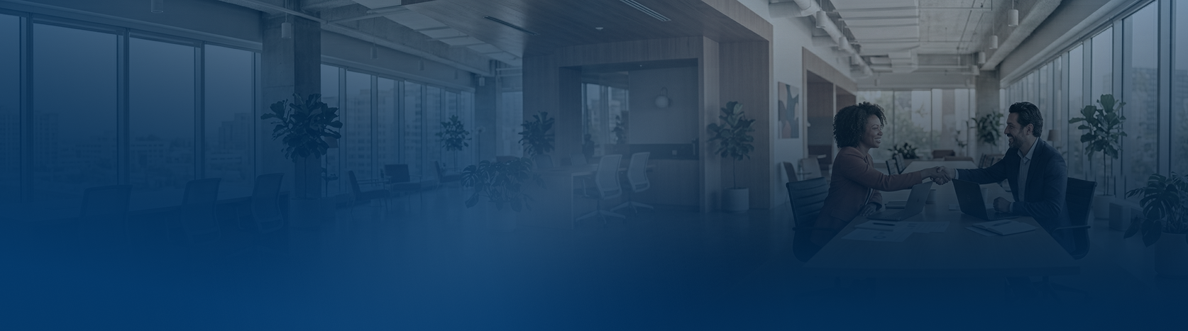 Dwóch ludzi uściski dłoni w biurze podczas spotkania przy stole z laptopami.