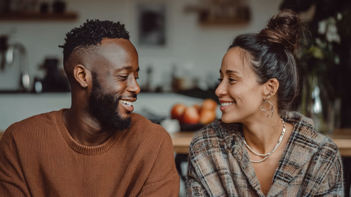 Smiling man and woman looking at each other indoors with blurred background.