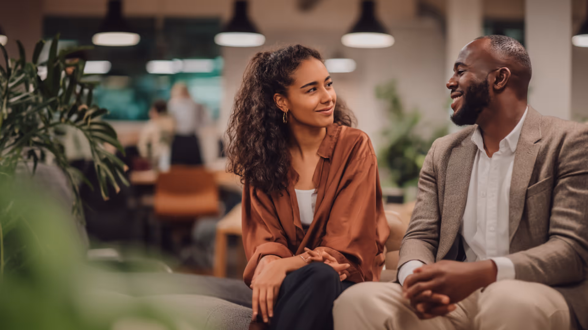 Smiling man and woman sitting and conversing in a modern office lounge area.