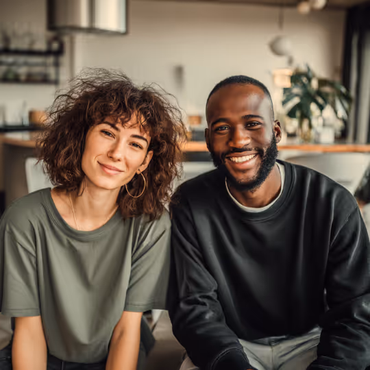 Smiling young woman with curly hair and man with beard sitting closely together indoors.