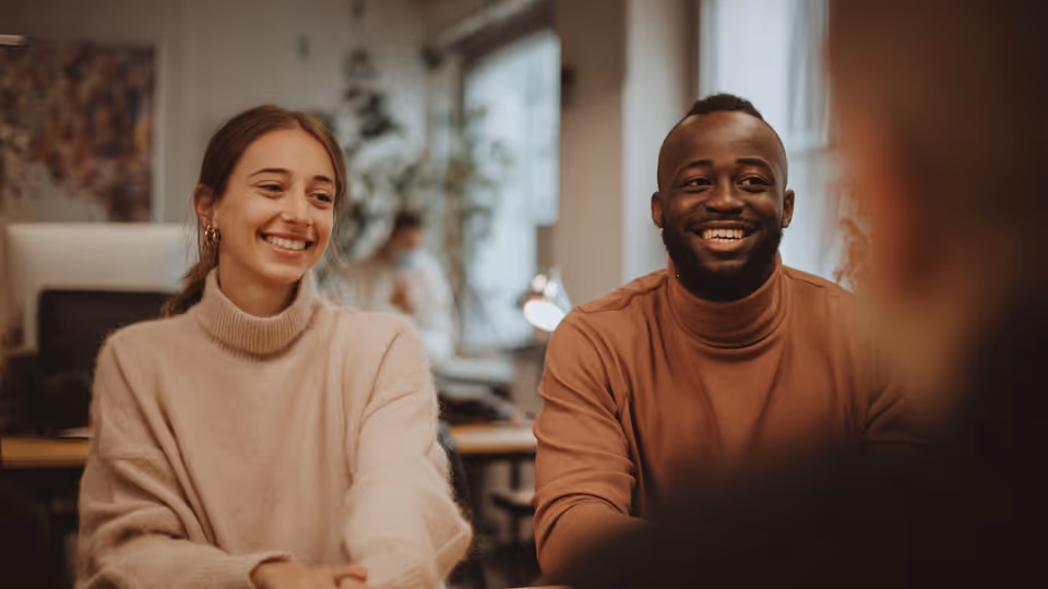Smiling young woman and man sitting side by side in an office setting.