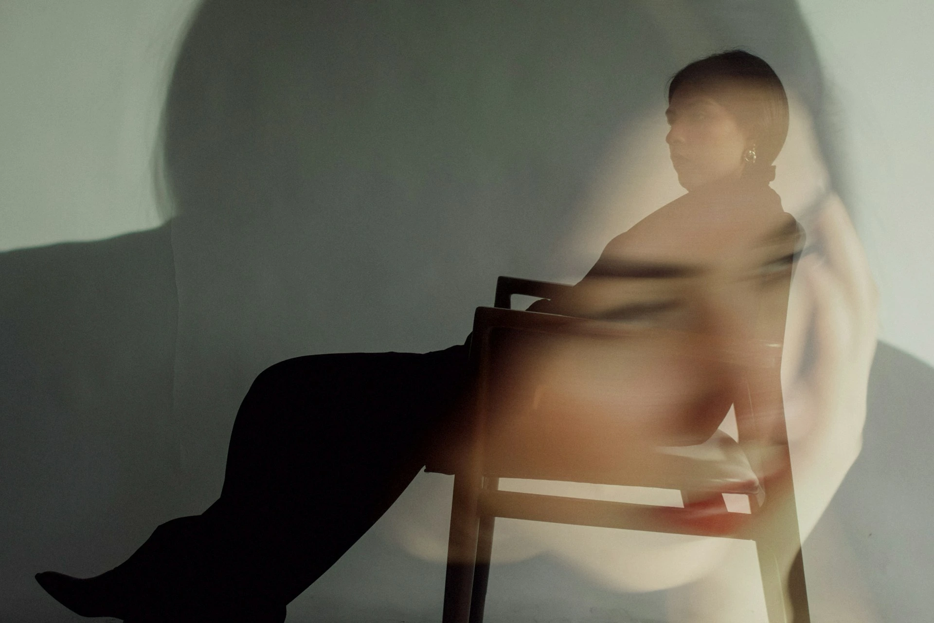Silhouette of a person sitting sideways on a chair with a blurred superimposed face overlay.