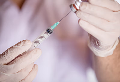Hands wearing gloves preparing a syringe with a vaccine or medication from a vial.