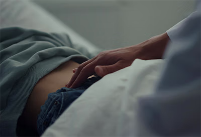 A hand gently resting on a person's lower abdomen while lying on a bed.