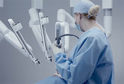 Surgeon in surgical scrubs and mask operating a robotic surgical system in a modern operating room.