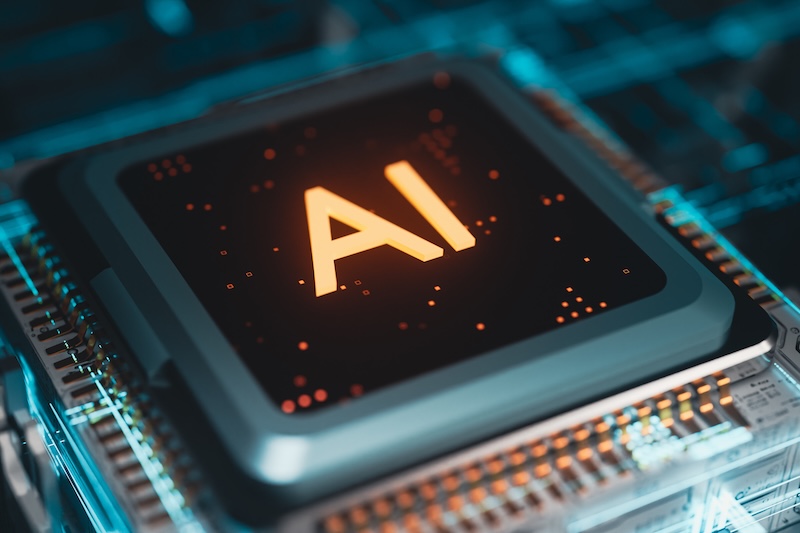A computer chip in a dark background with bright orange letters "AI". 