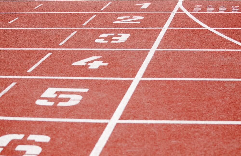 A close up of a running track with lane numbers in white. 