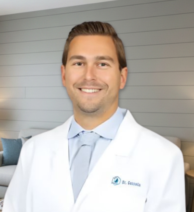 Dr. Max Gosselin, a trusted dentist at Gasior Family Dental in Northville, MI, smiles warmly in his professional portrait while wearing a white lab coat and tie. His approachable expression reflects a commitment to patient-centered care, clinical excellence, and creating a comfortable dental experience for individuals and families of all ages.