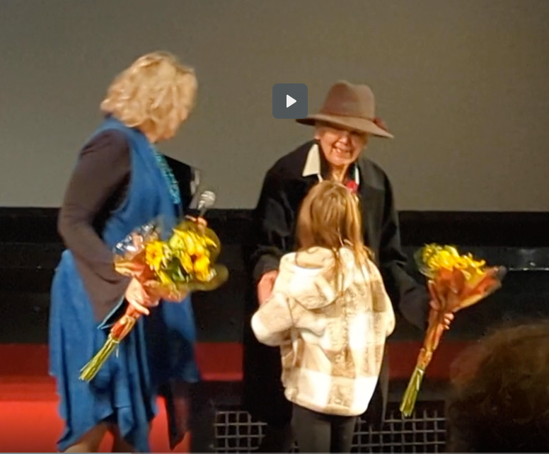 A child presents flowers to two people