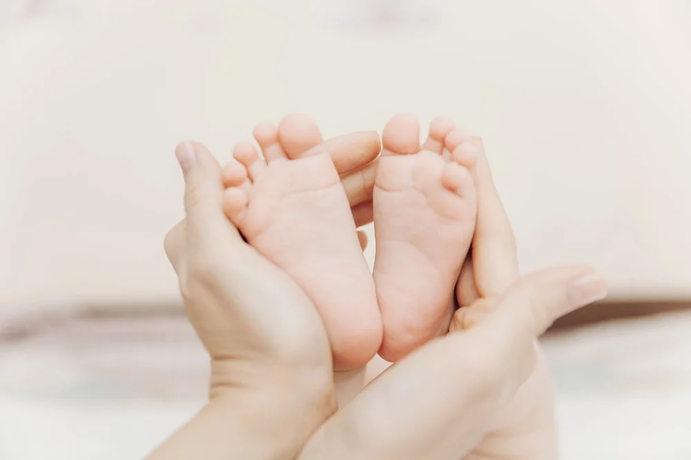 Adult hands gently holding the feet of a newborn baby against a soft background.