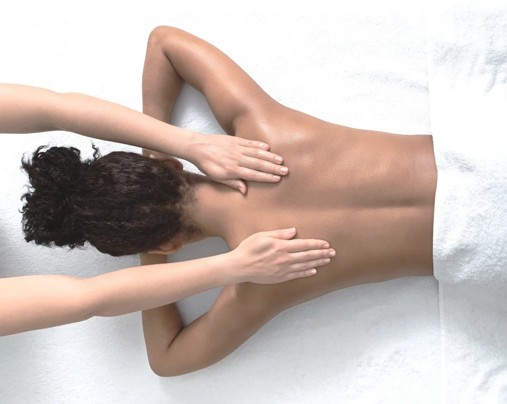 Person receiving a back massage while lying face down on a white towel.