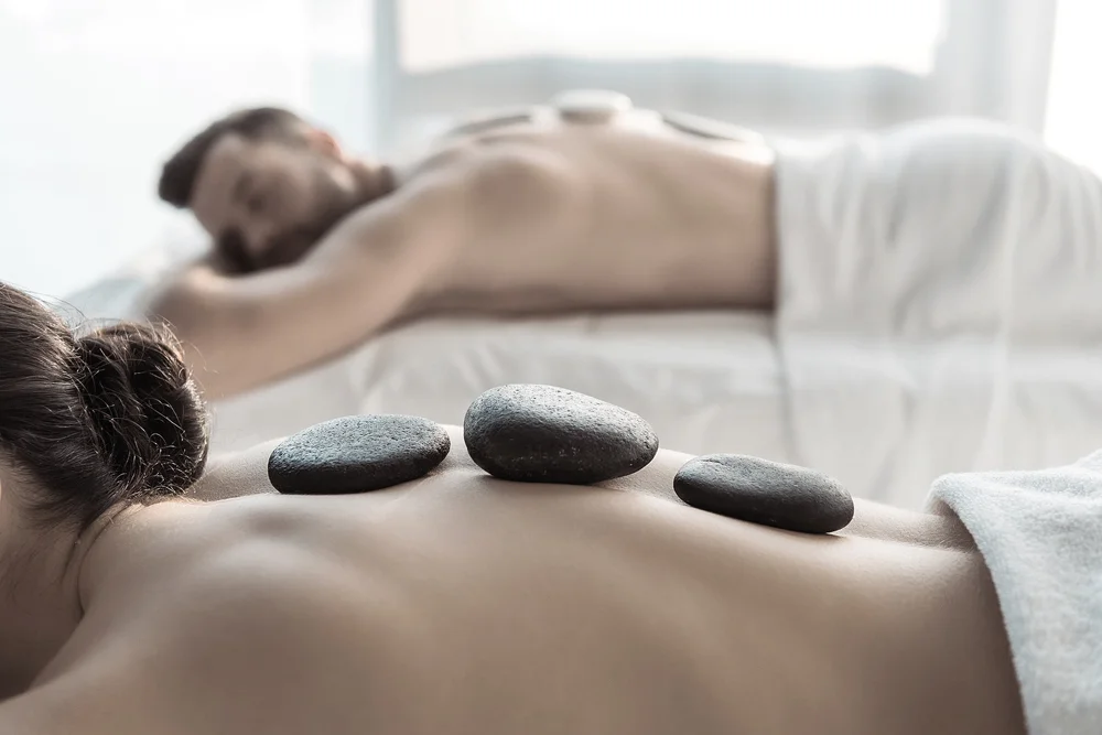 Man and woman lying face down with hot stones on their backs during a spa massage.