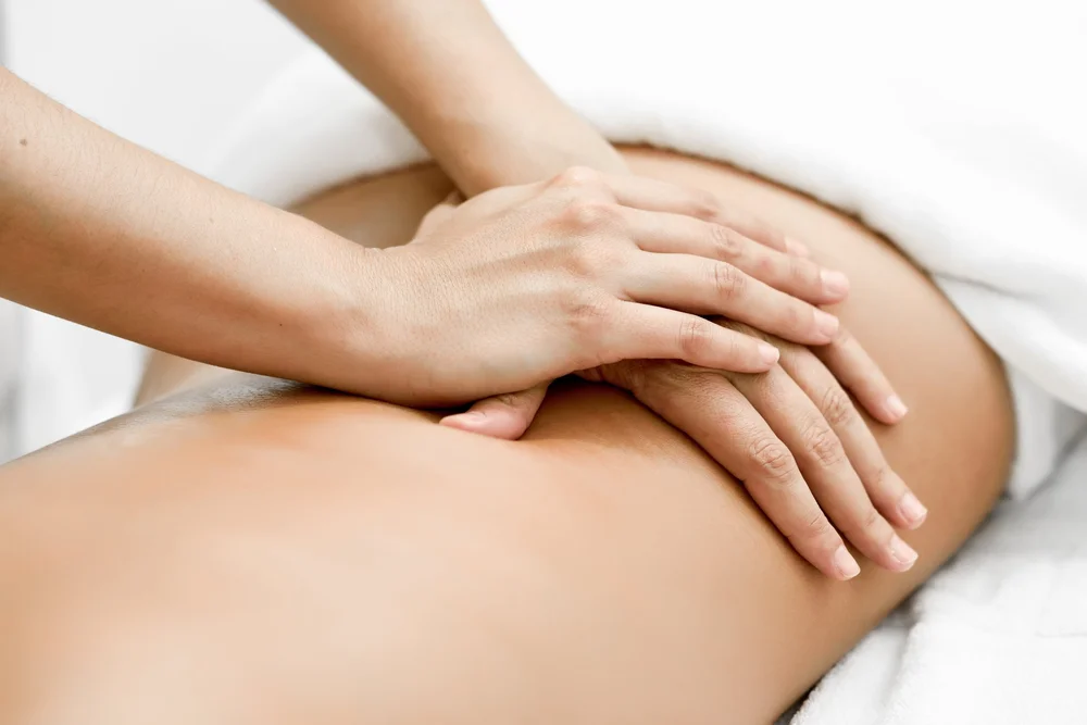 Two hands performing a massage on a person's bare back covered partially with a white towel.