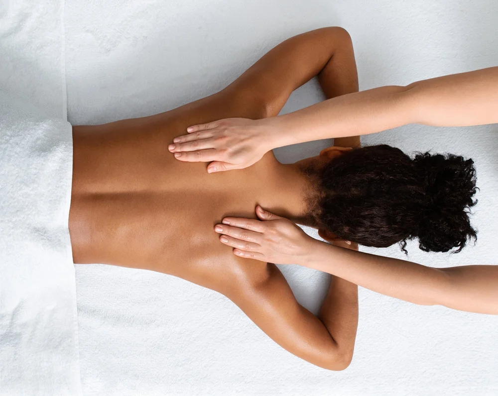 Person receiving a back massage while lying face down on a white towel-covered surface.