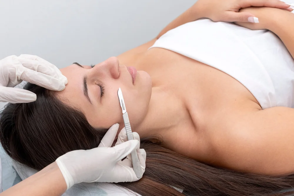 Woman receiving dermaplaning treatment on her cheek by a professional wearing white gloves.
