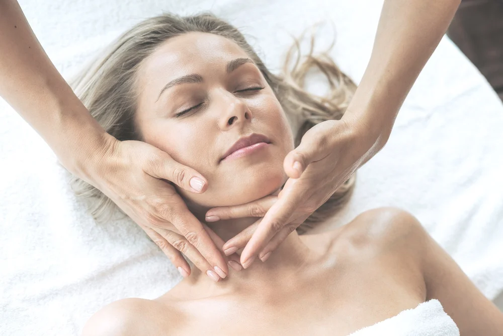 Woman receiving a facial massage with closed eyes on a white towel.