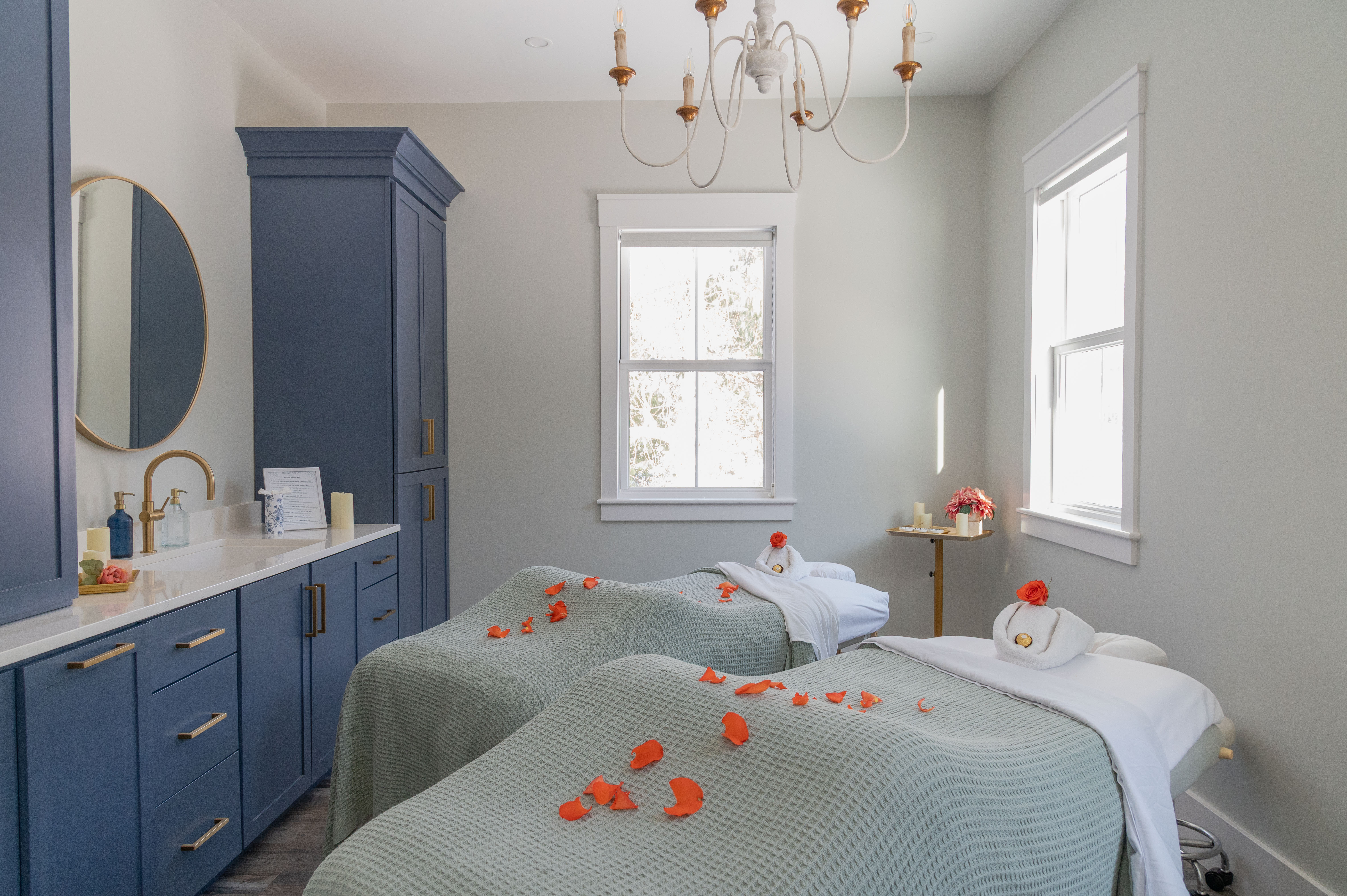 Spa room with two massage tables covered in gray blankets and scattered orange flower petals.