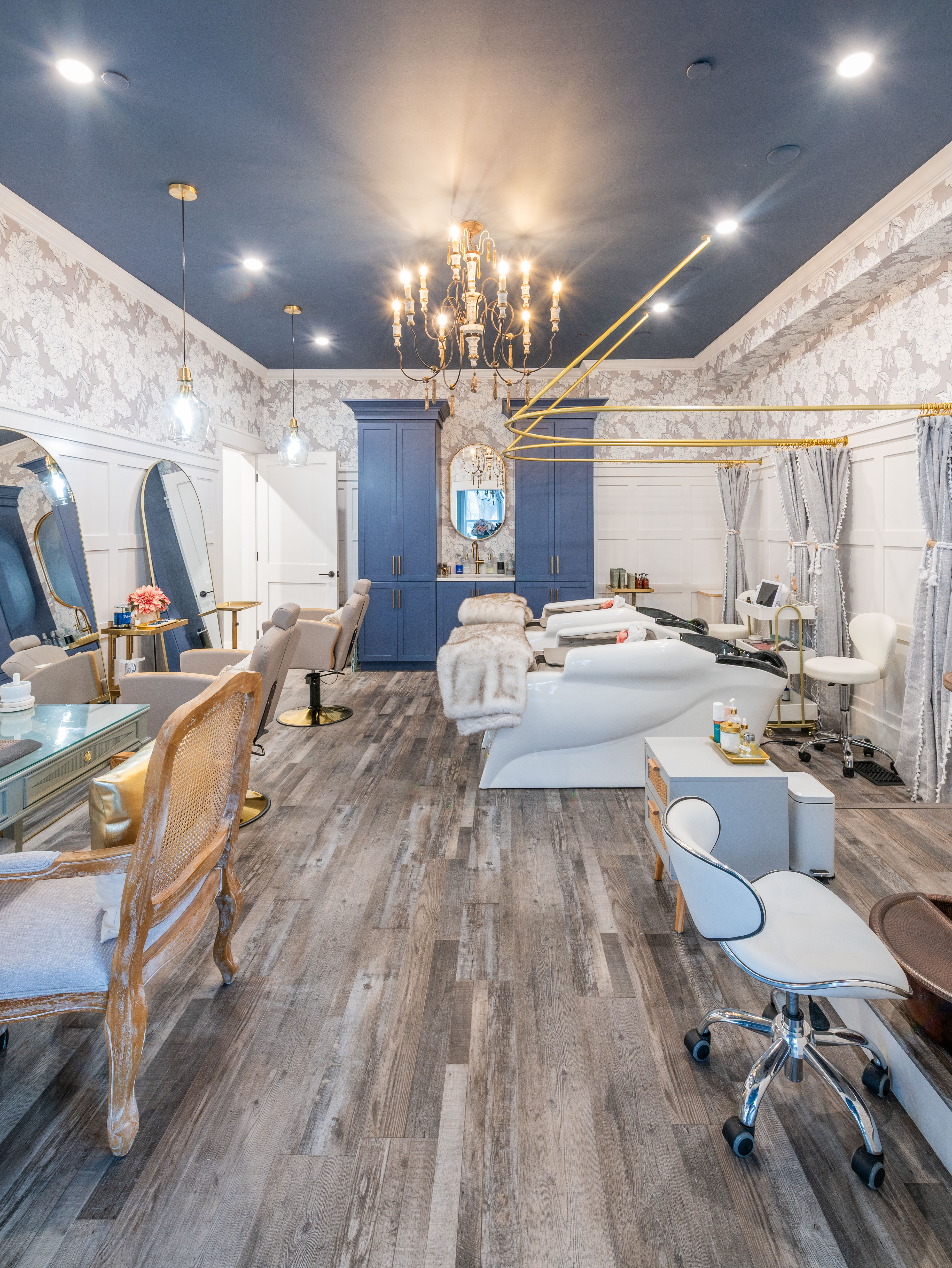 Stylish salon with blue ceiling, chandelier, white wash basins, chairs, and wood-patterned floor.