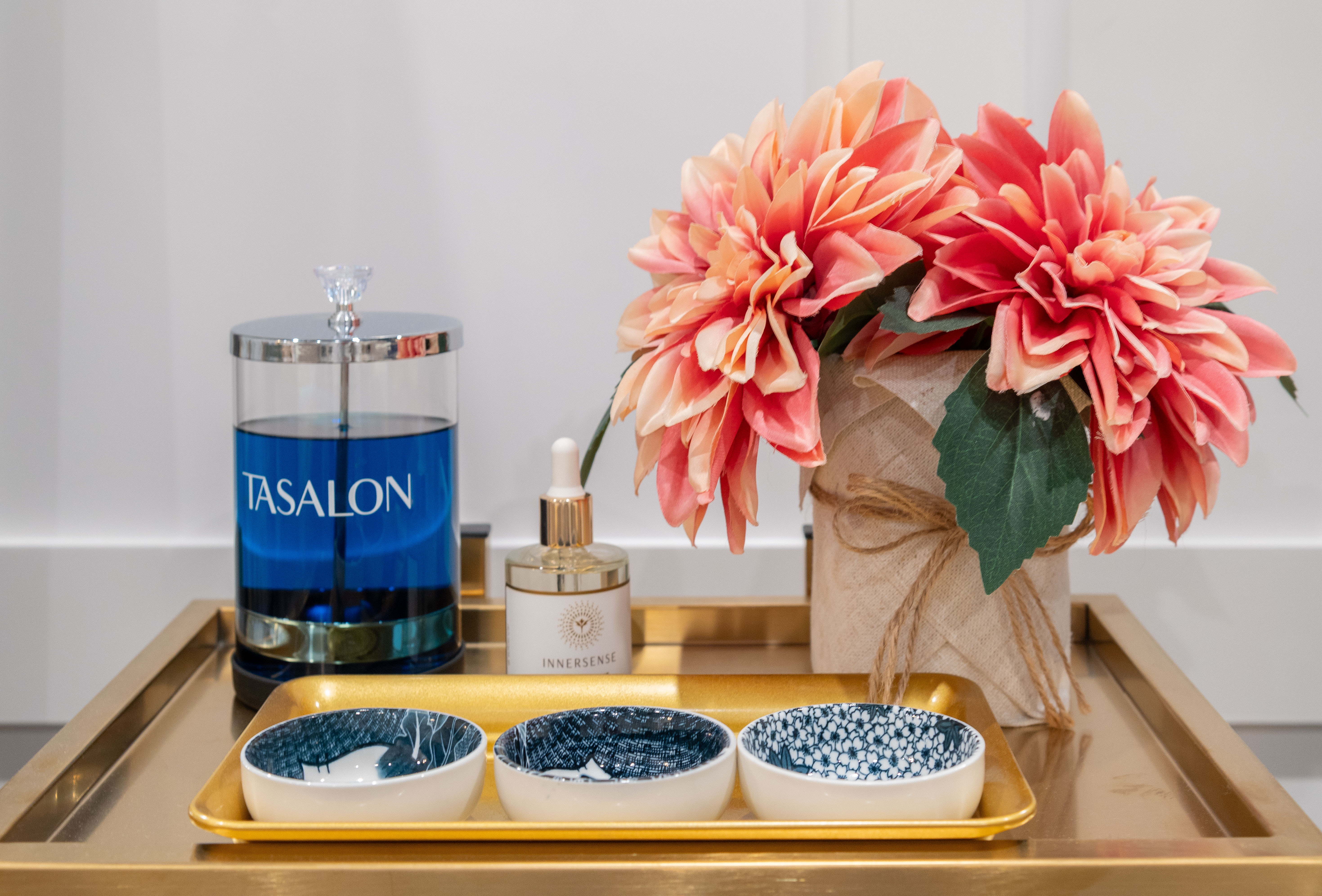 Tray with three small patterned bowls, a floral arrangement, a blue TASALON container, and an INNERSENSE bottle.