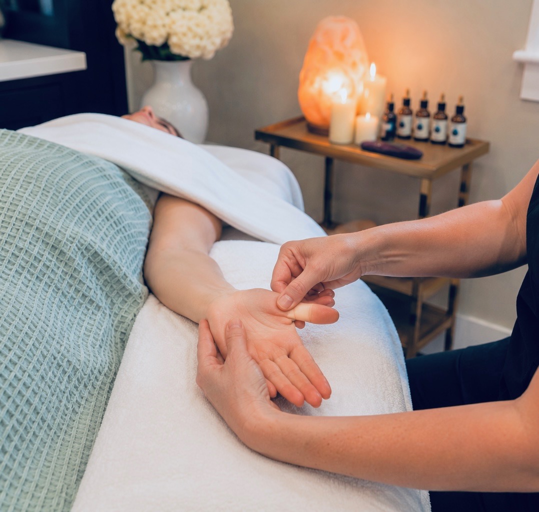 A person receives a hand massage on a spa bed with candles and essential oils in background.