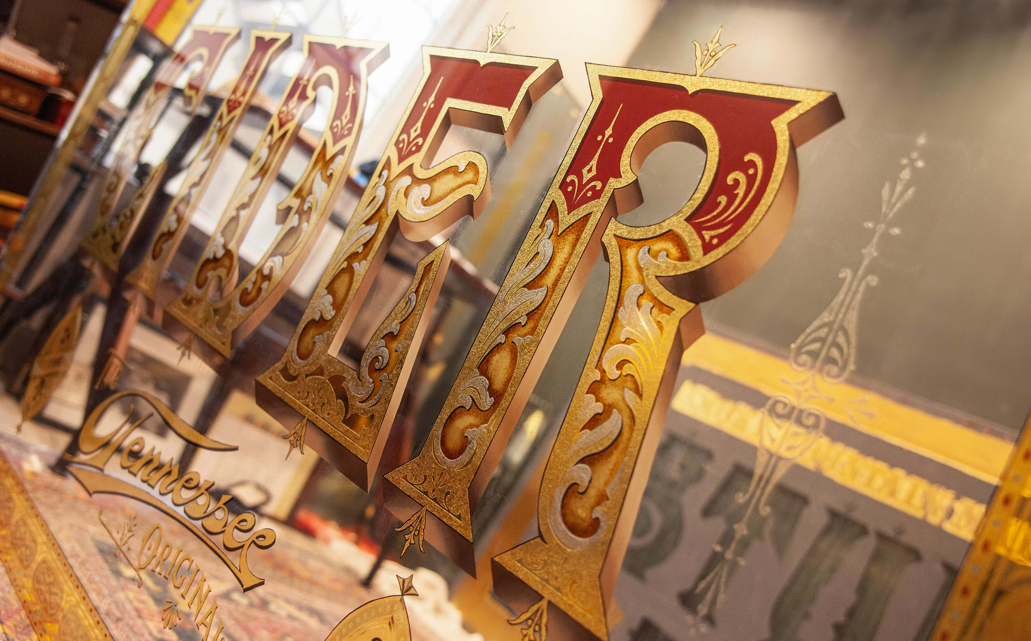 Close-up of a decorative glass window or mirror panel with ornate gold and red lettering spelling 'PILGR' and the word 'Tennessee' below in cursive.