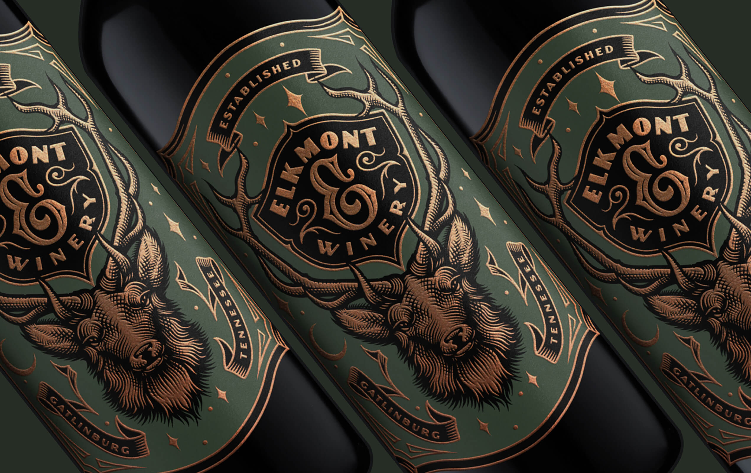 Close-up of three dark wine bottles with green labels featuring a detailed copper-colored elk head and antlers, and text reading 'Elkmont Winery', 'Established', 'Tennessee', and 'Gatlinburg'.