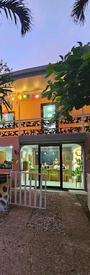 Two people behind a wooden counter inside a warmly lit two-story building at dusk.