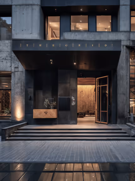Modern hotel entrance with black facade, illuminated sign reading 'THE GRID', and open glass door showing wooden interior.