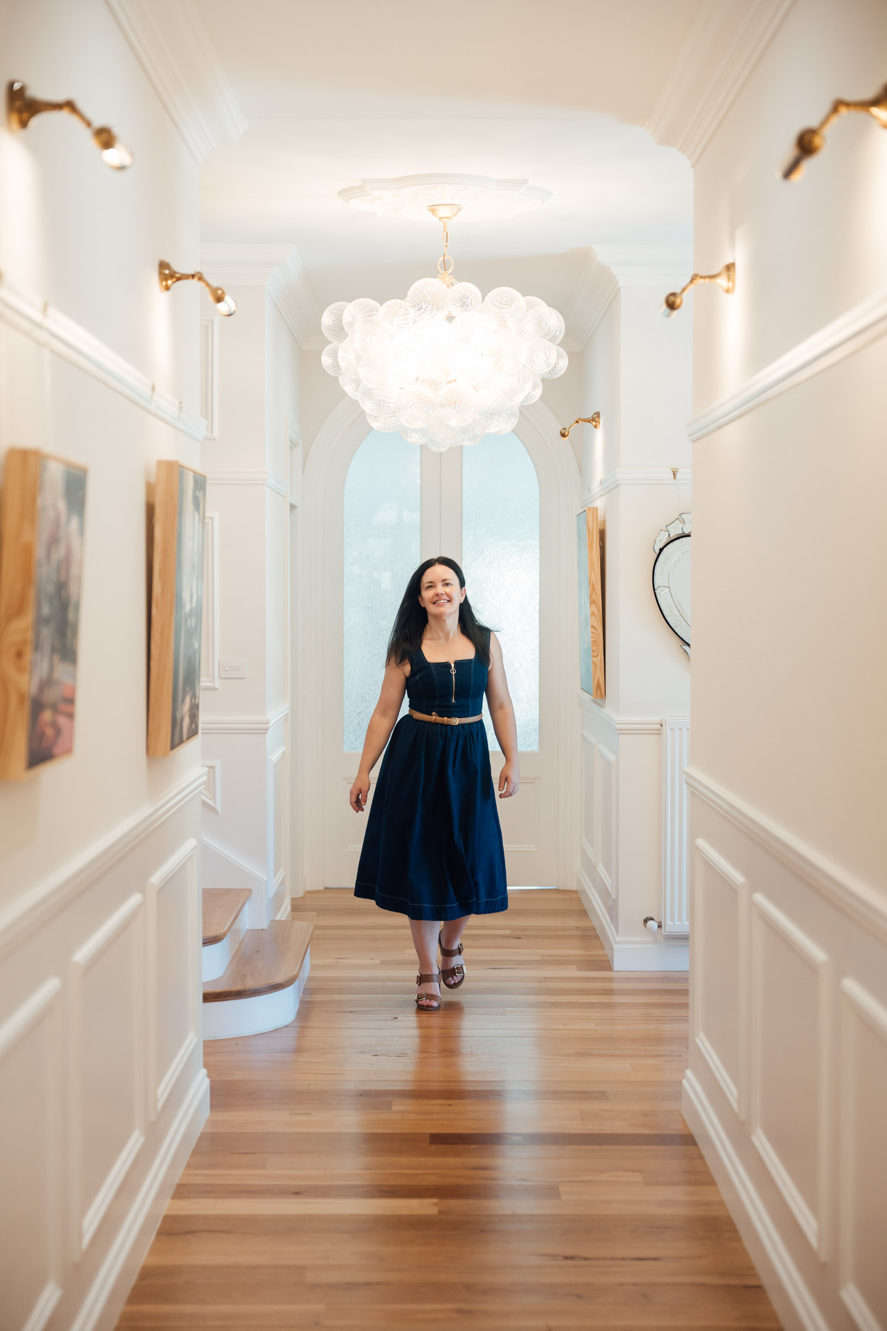 Woman in a navy blue dress walking down a bright hallway with wooden floors and white walls.