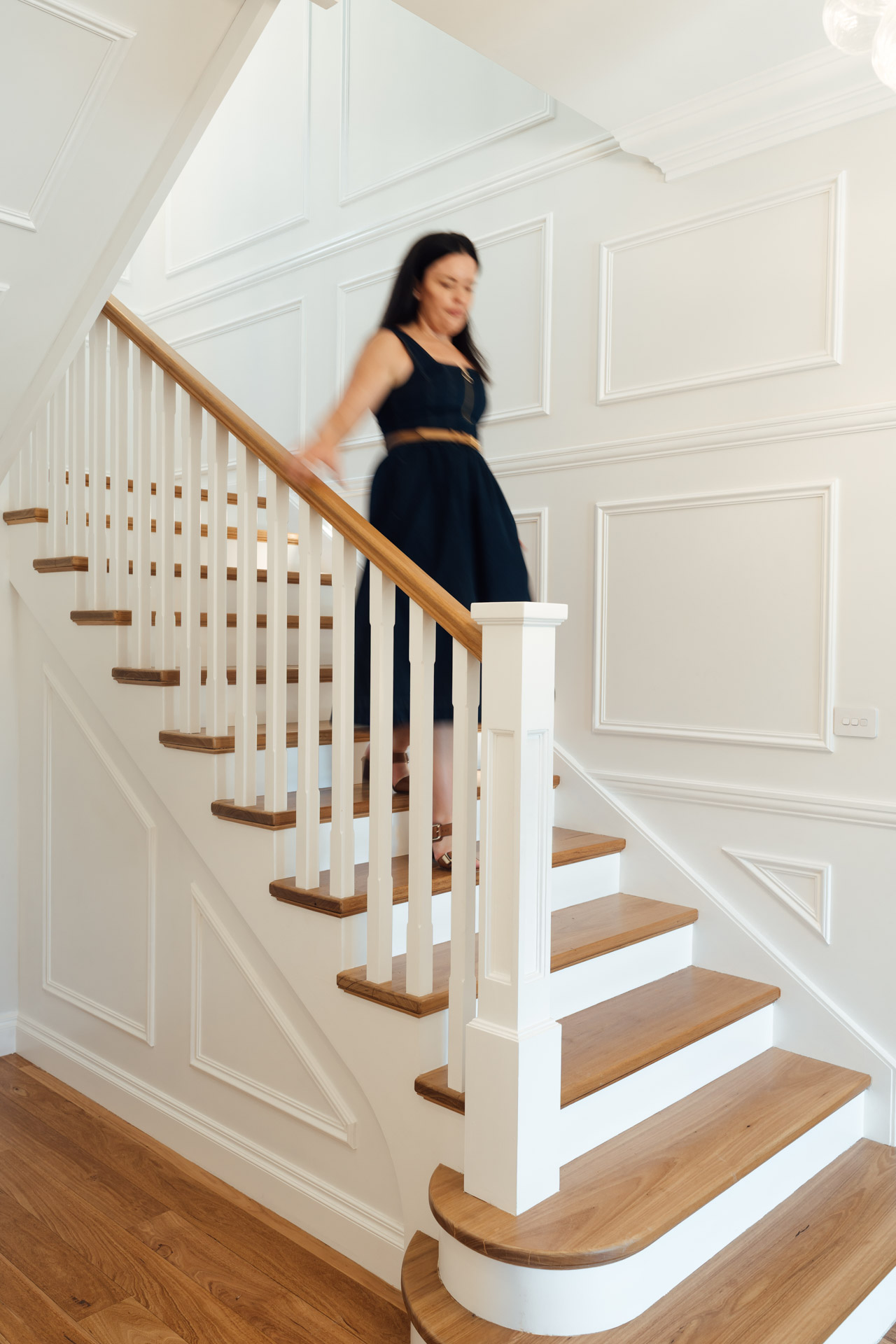 Woman in a black dress descending white wooden stairs with wooden treads in a bright interior.