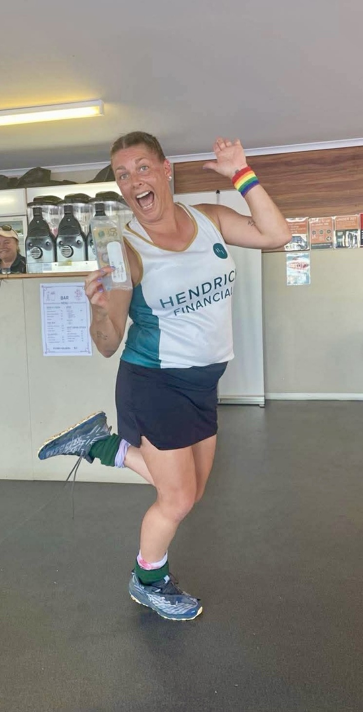 Woman wearing a Hendrick Financial tank top and rainbow wristband joyfully holding a $50 bill indoors.