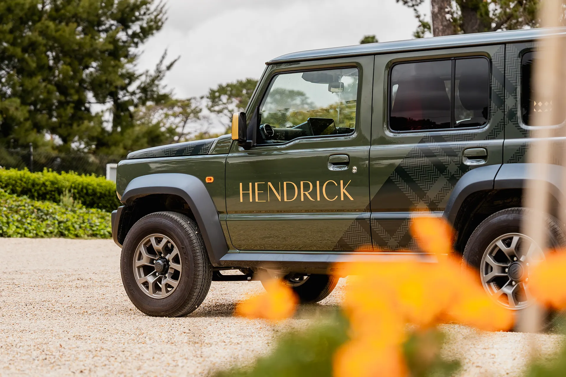Side view of a green SUV with the word HENDRICK on the door, parked on a gravel surface.