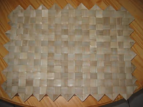 Handwoven placemat with a square pattern on a wooden surface.
