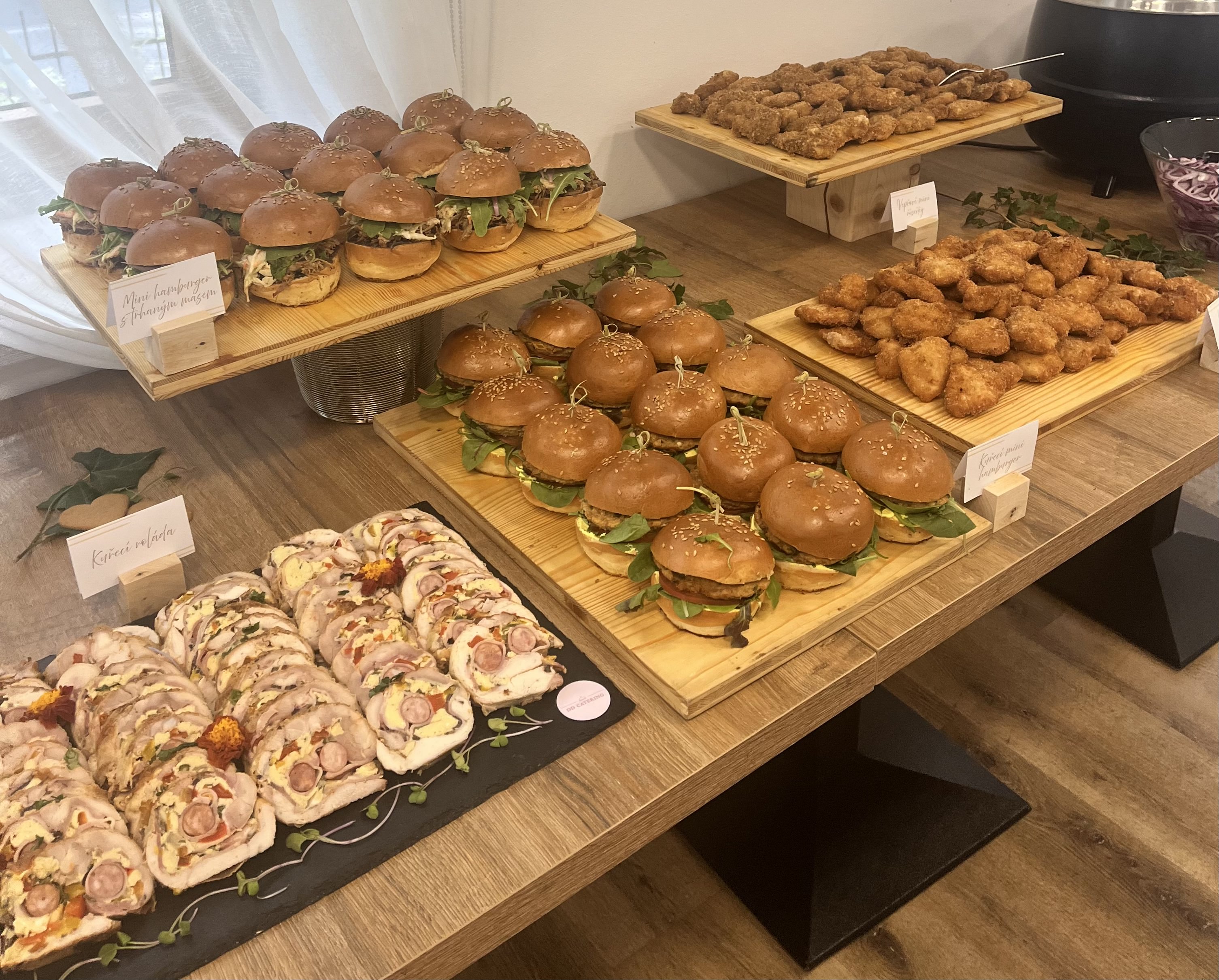 Stůl s různými mini sendviči, kousky smaženého kuřete a roládami z kuřecího masa ozdobenými bylinkami.