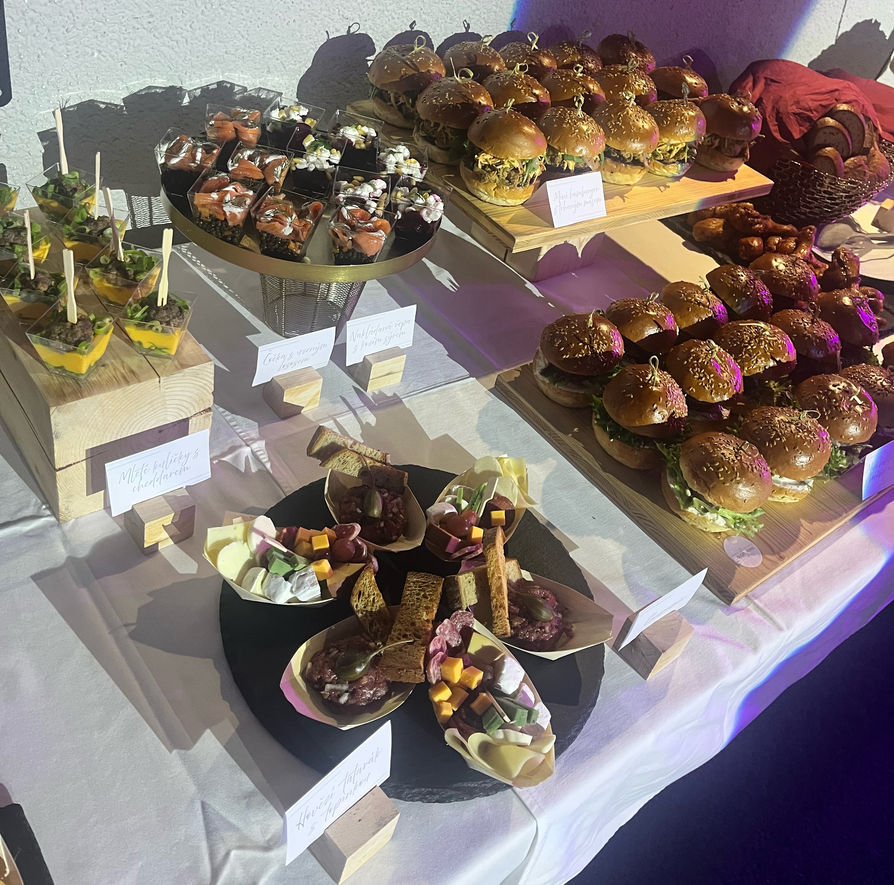 Bufet se zakusek na stole obsahujici caprese poharky, mistnost salat a male brambory s kvetinami a syrovym kremem.