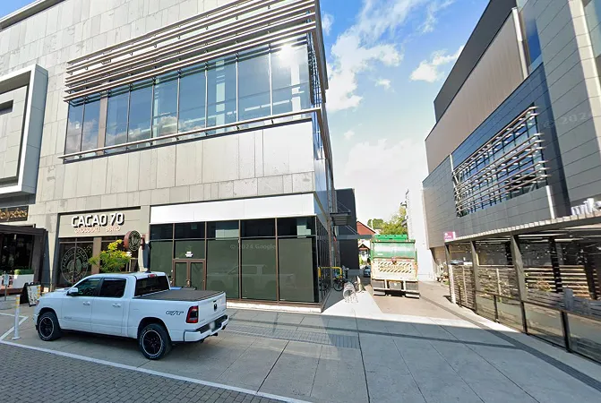 White pickup truck parked next to a modern building with a sign reading 'CACAO 70 Chocolat' under a partly cloudy sky.