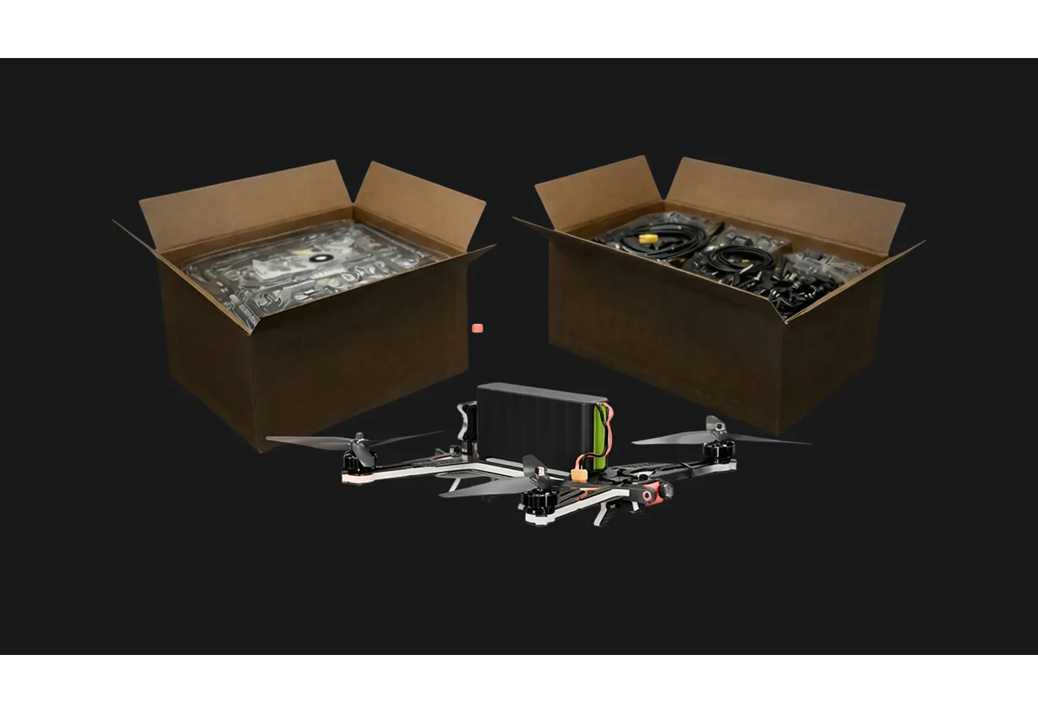 Quadcopter drone with four propellers and battery, positioned between two open cardboard boxes containing drone parts and cables.