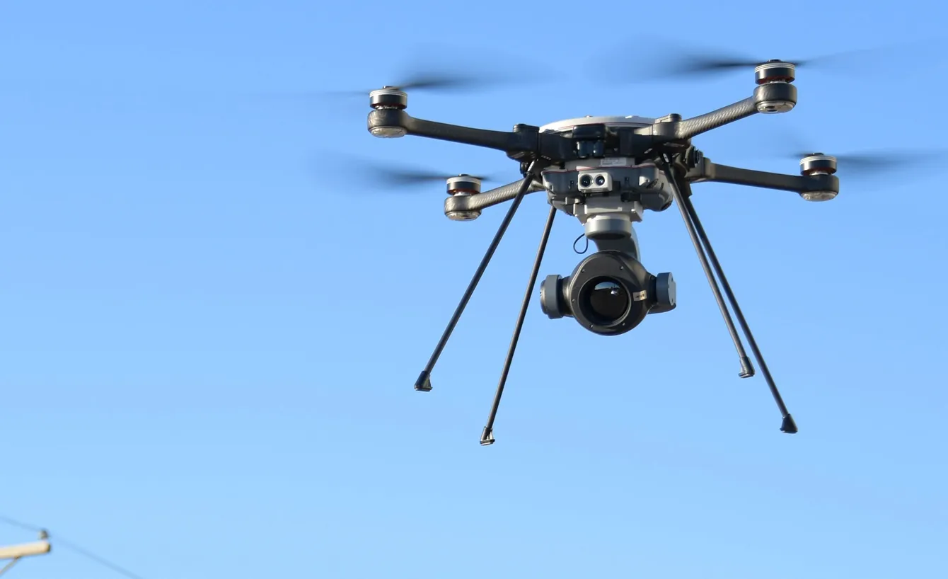 Close-up of a professional drone with a camera hovering against a clear blue sky.