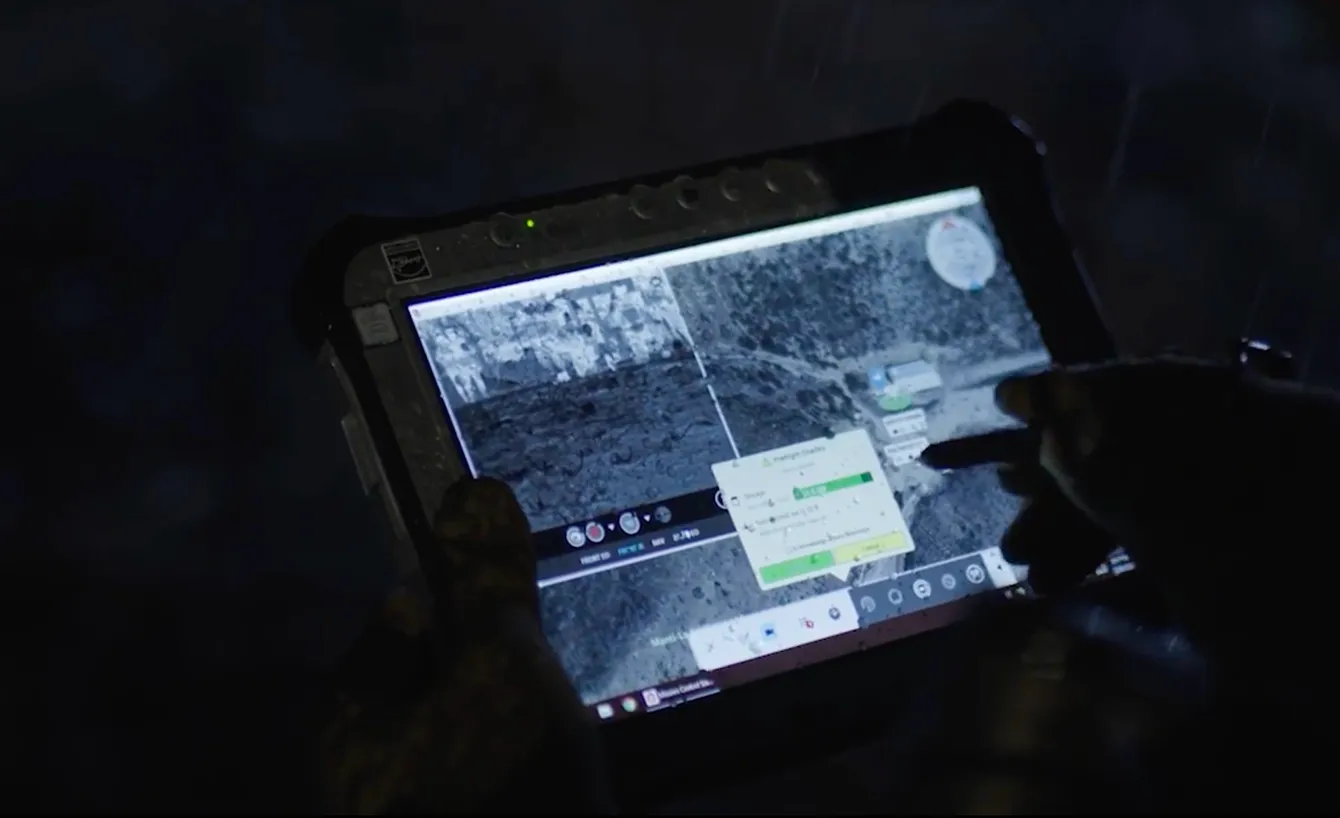 Person using a rugged tablet with stylus to interact with a digital map or satellite imagery interface in low light.