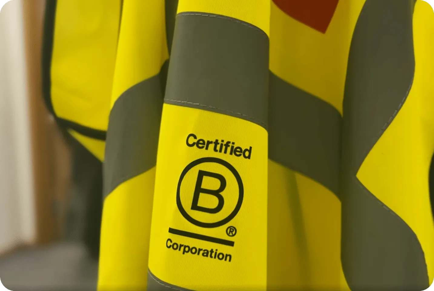 Yellow and gray safety jacket with a 'Certified B Corporation' logo printed on the sleeve.