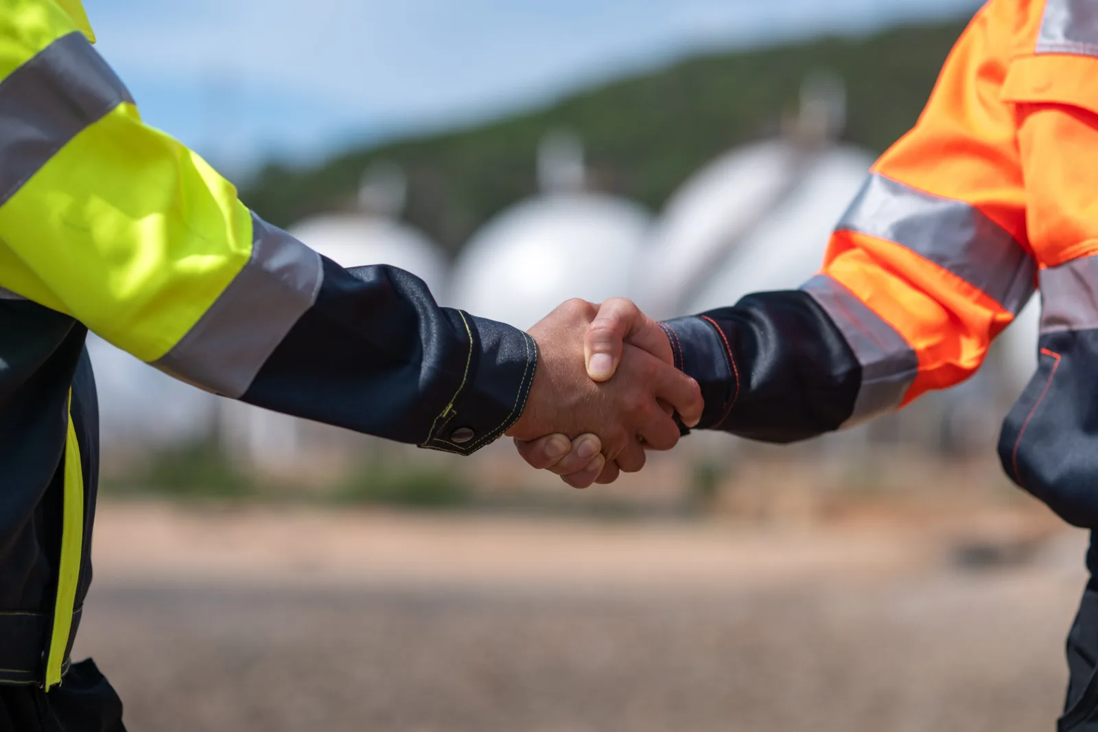 Two site workers in high visibility workwear shaking hands at an industrial site