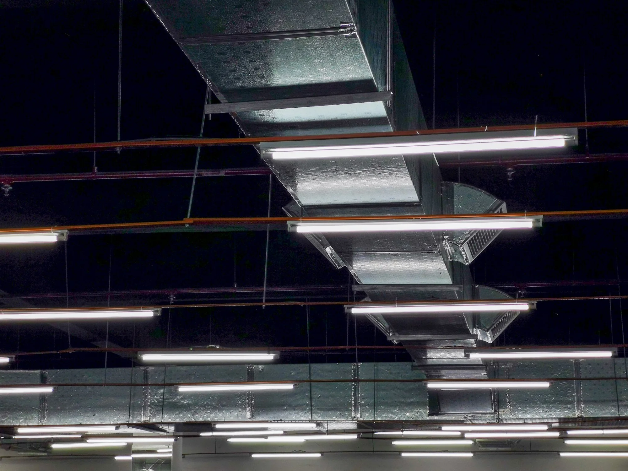Rows of fluorescent tube lights suspended from an industrial ceiling, illustrating mercury-containing lamps that require compliant hazardous waste disposal