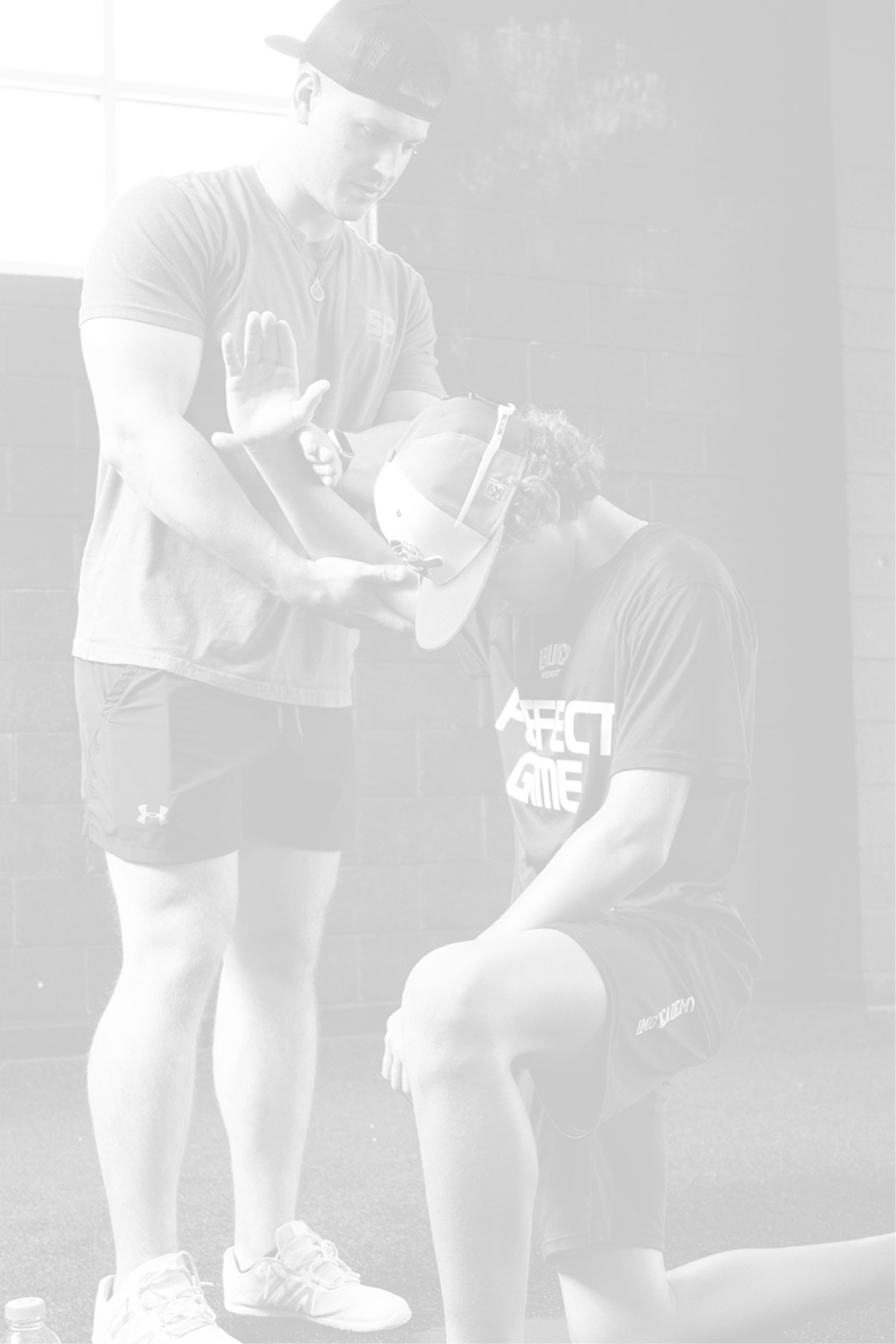 Trainer assisting a young athlete with arm stretching in a gym with black walls.