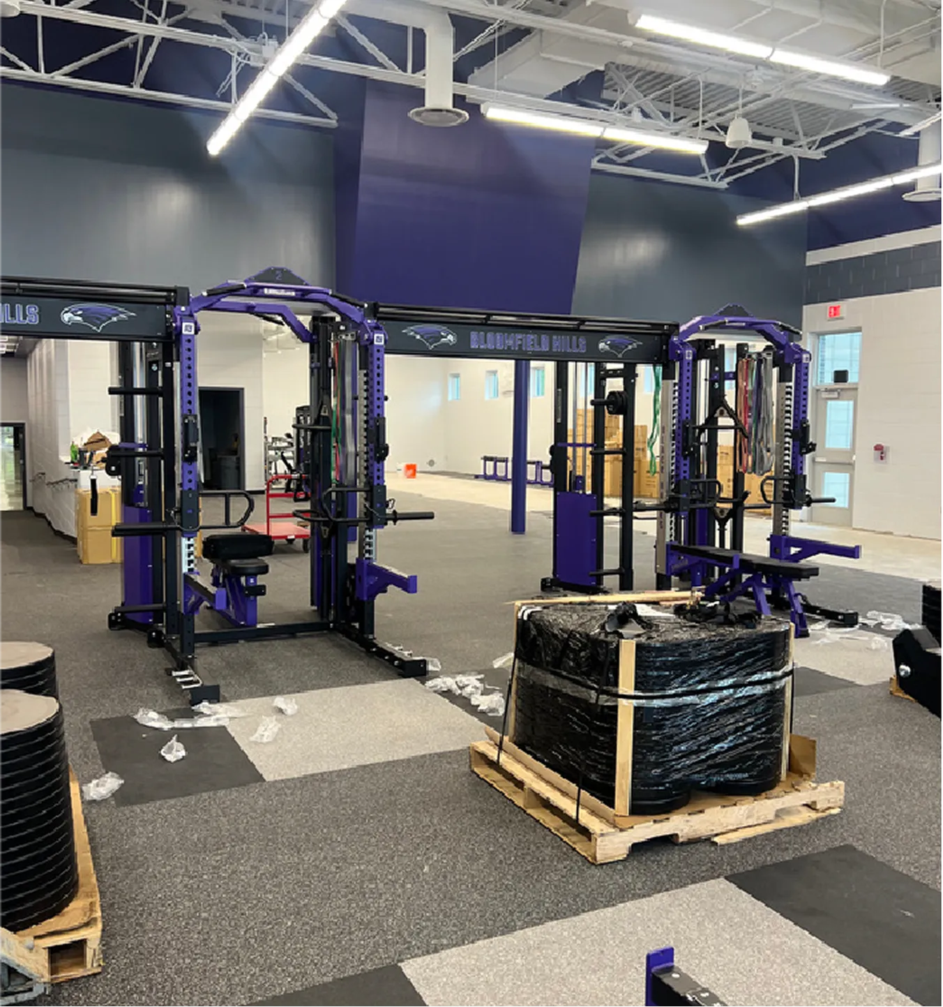 New gym weightlifting stations labeled Bloomfield Hills with packed weight plates on pallets.