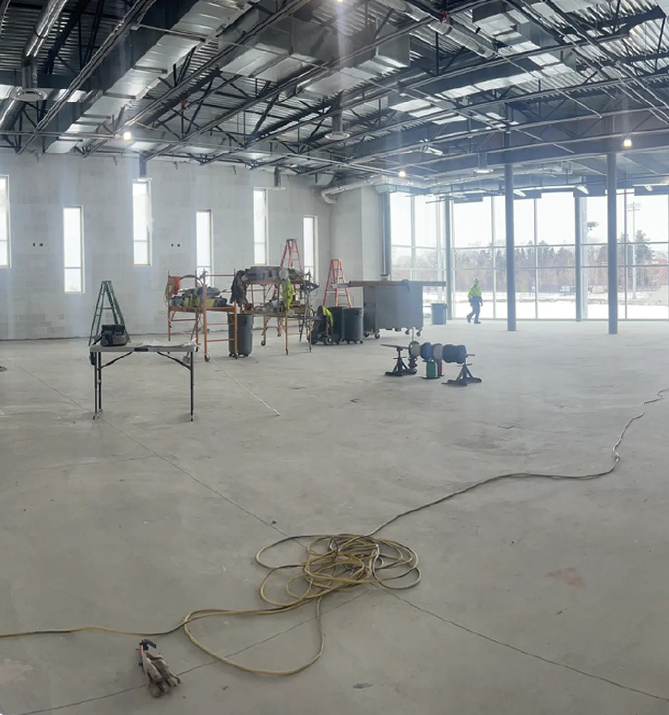 Large industrial room under construction with scaffolding, ladders, cable on floor, and workers inside.