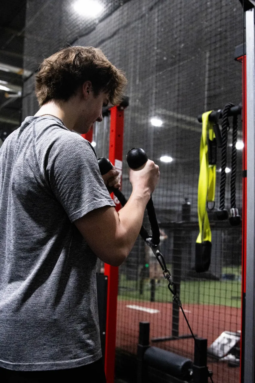 A baseball or softball player working on their arm connection and swing sequence using a cable machine. Similar sport-specific training aids are available at equipment retailers like Real Feel Sports.