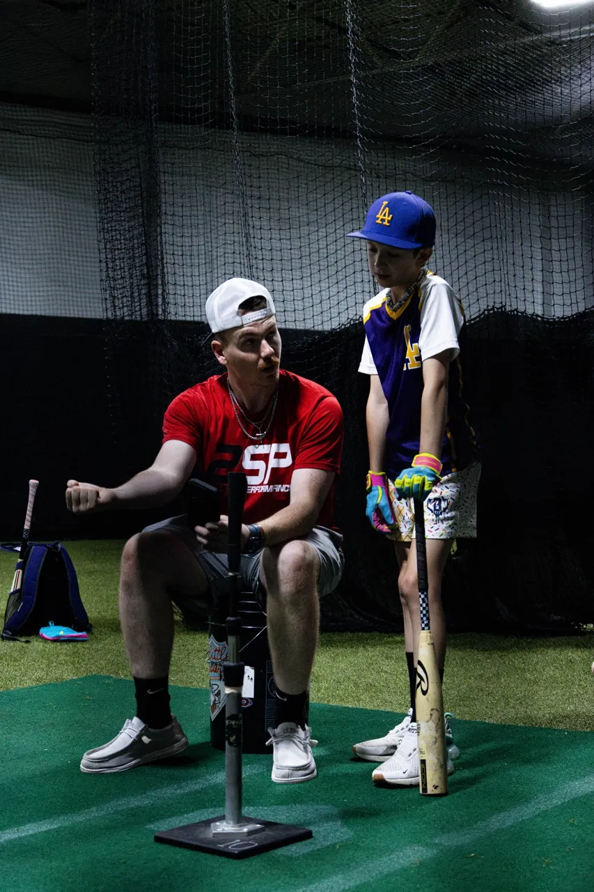 Baseball coach running a hitting drill for a young player at 2SP Fieldhouse in Michigan.