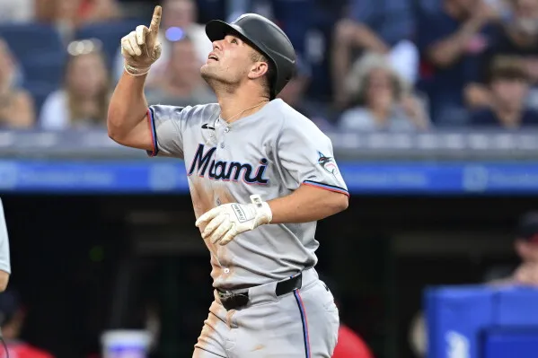 Miami baseball player in gray uniform points upward during a game at a stadium.