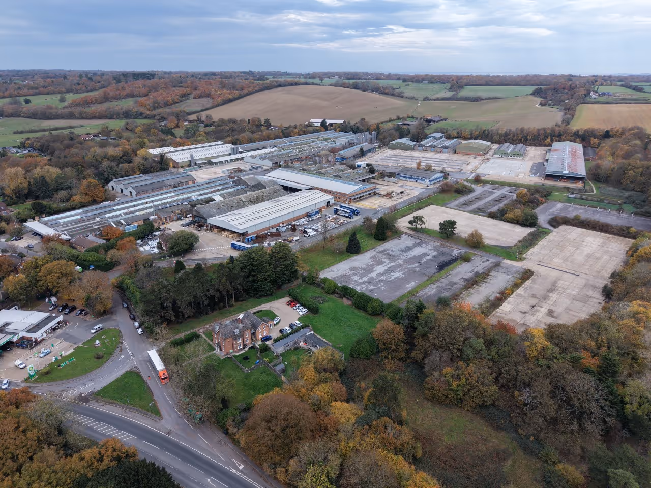 Aerial view of a large industrial complex with multiple warehouses, surrounded by trees and fields under a cloudy sky.